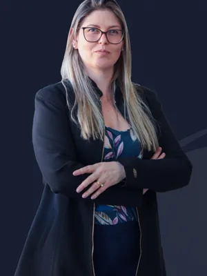 Retrato de Dieisa Ribeiro, contadora, de blazer preto e óculos, com os braços cruzados